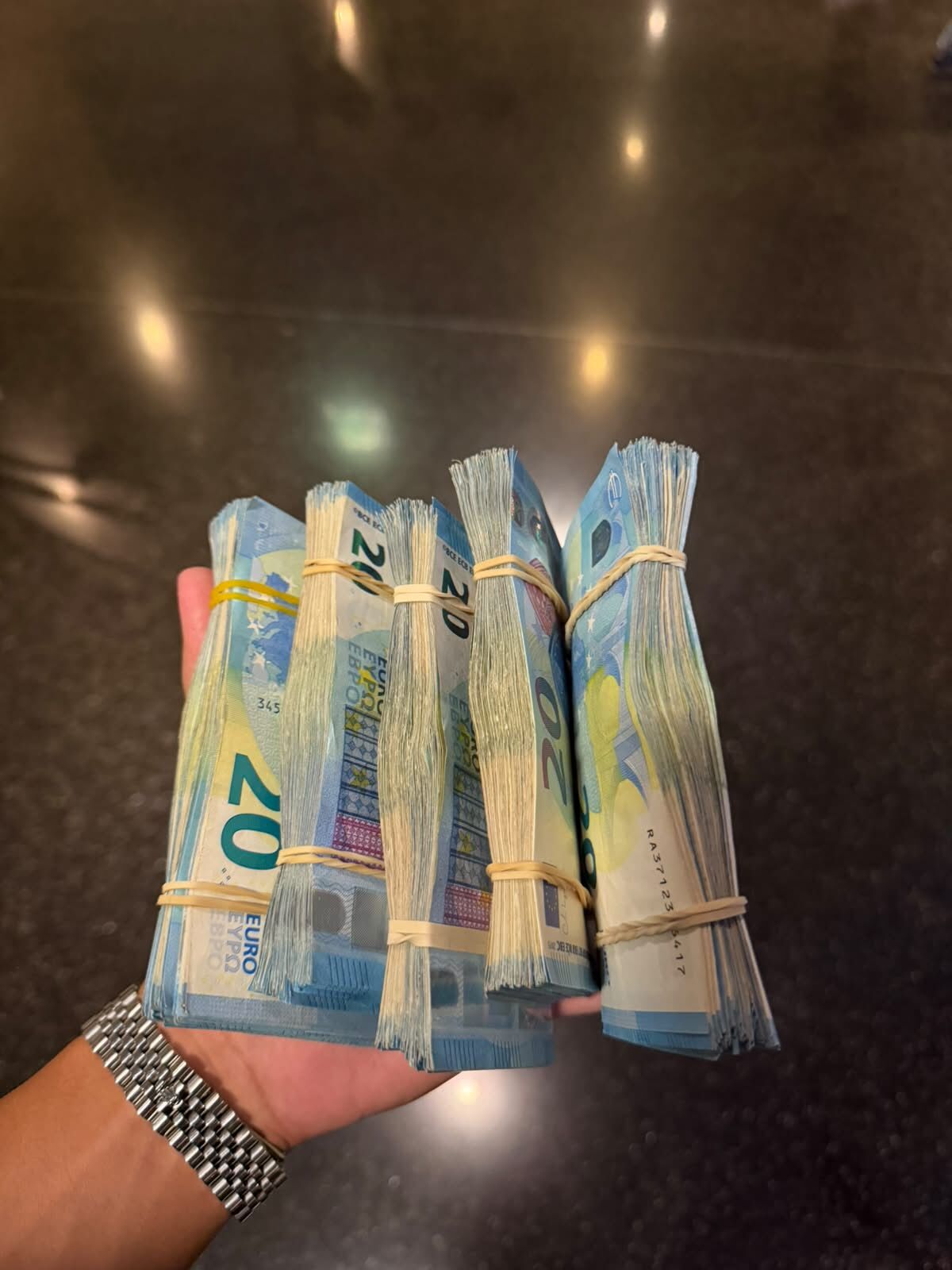 Mão com cinco maços de notas de 20 euros e relógio de aço
